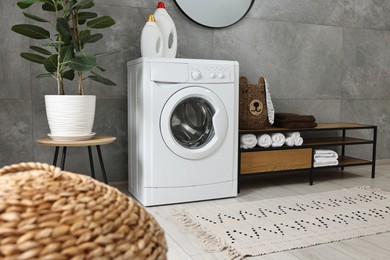 Photo of Washing machine, detergents, houseplant, baskets and storage cabinet in laundry room