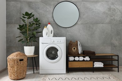 Photo of Washing machine, detergents, houseplant, baskets and storage cabinet in laundry room