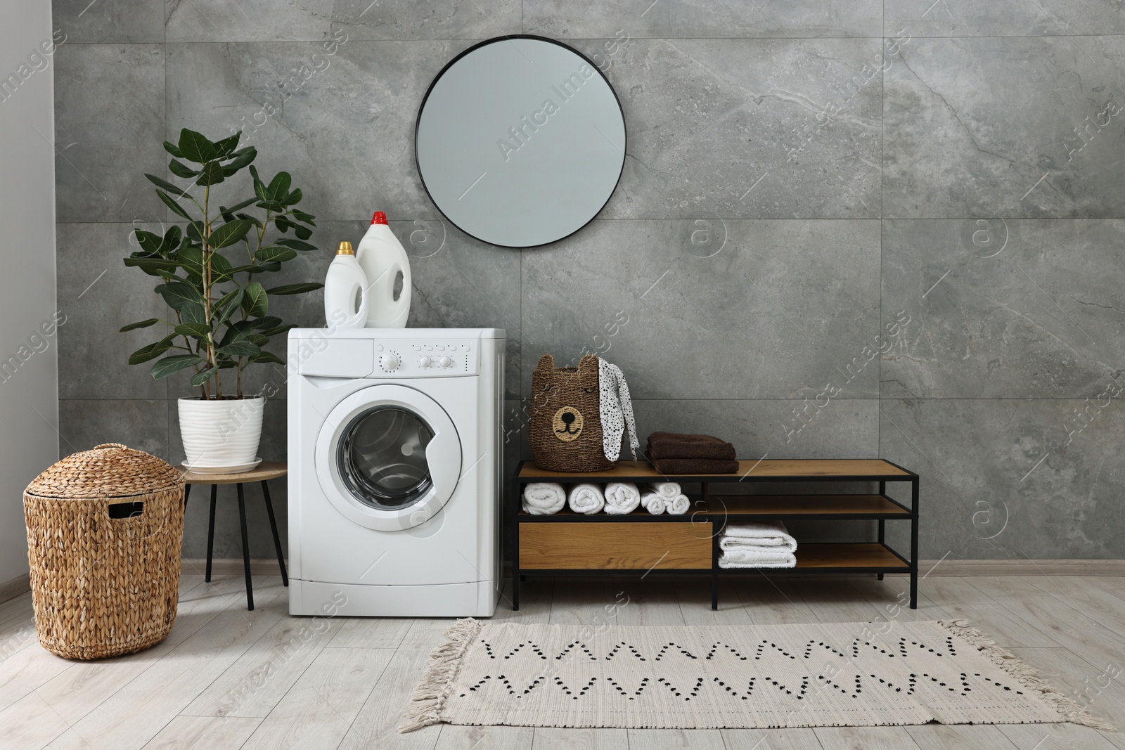 Photo of Washing machine, detergents, houseplant, baskets and storage cabinet in laundry room