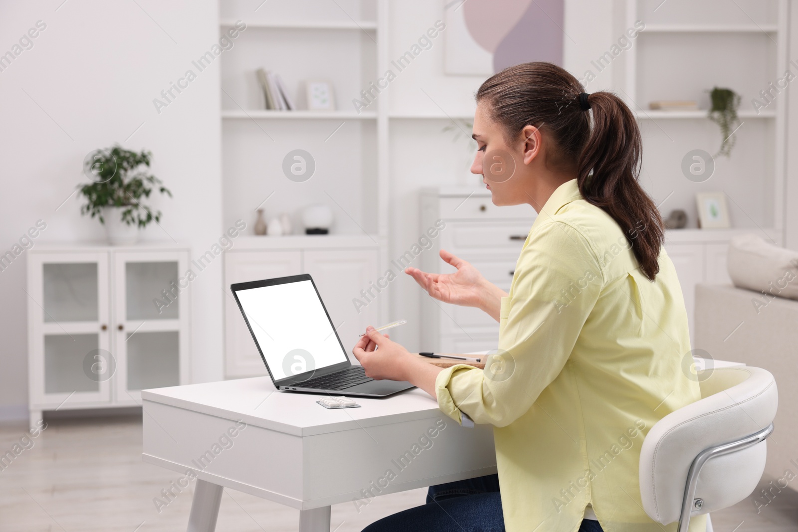 Photo of Sick woman with thermometer having online consultation with doctor via laptop at white table indoors