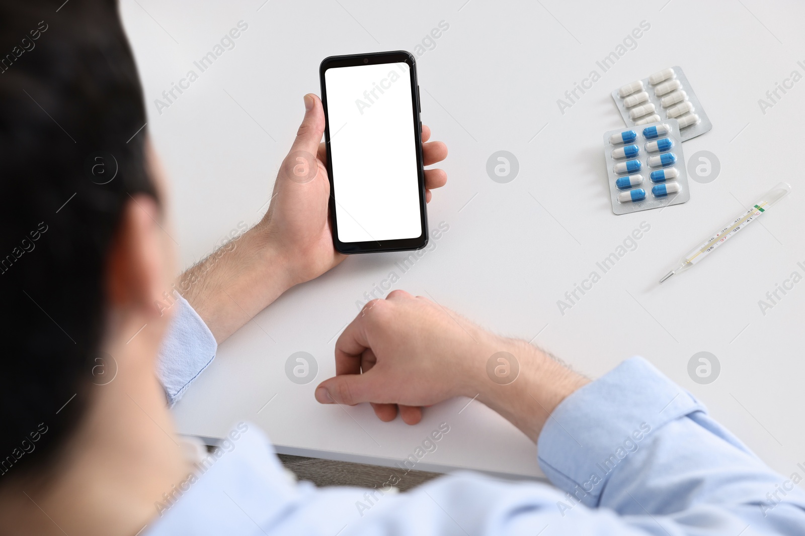 Photo of Sick man having online consultation with doctor via smartphone at white table indoors, closeup