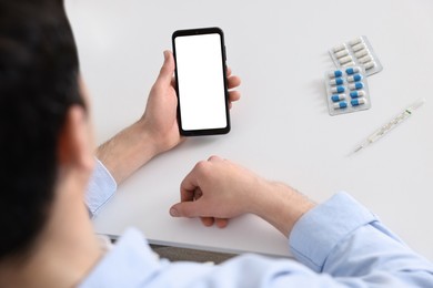 Photo of Sick man having online consultation with doctor via smartphone at white table indoors, closeup