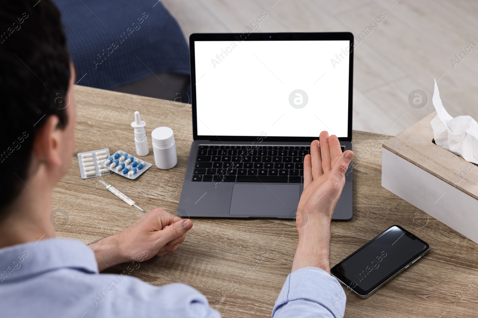 Photo of Sick man having online consultation with doctor via laptop at wooden table indoors