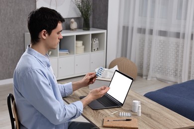 Photo of Sick man with pills having online consultation with doctor via laptop at wooden table indoors