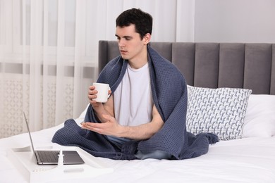 Photo of Sick man with cup having online consultation with doctor via laptop at home