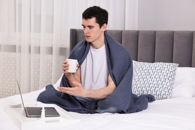 Sick man with cup having online consultation with doctor via laptop at home