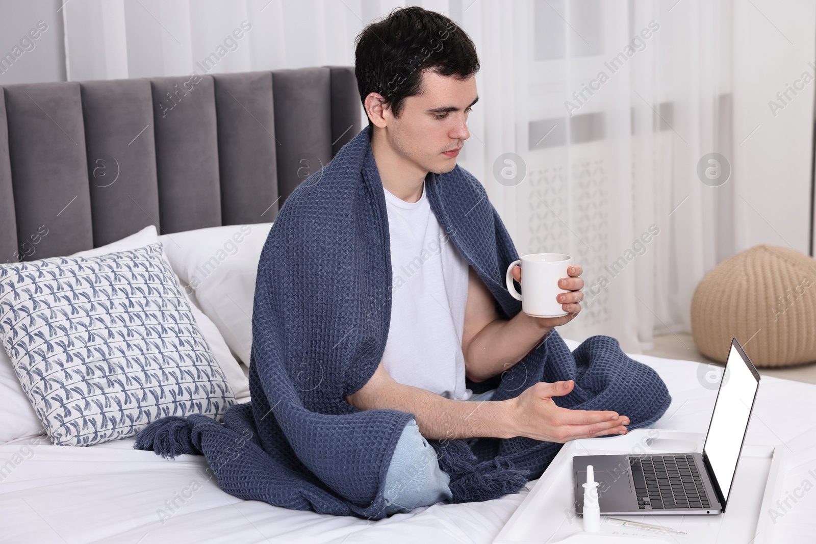 Photo of Sick man with cup having online consultation with doctor via laptop at home