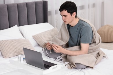 Photo of Sick man with thermometer having online consultation with doctor via laptop at home