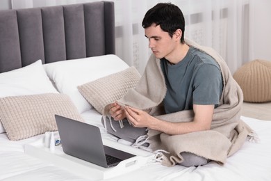 Sick man with thermometer having online consultation with doctor via laptop at home