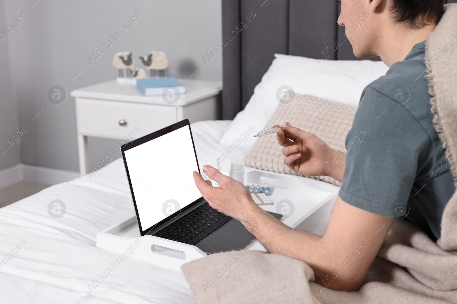 Photo of Sick man with thermometer having online consultation with doctor via laptop at home