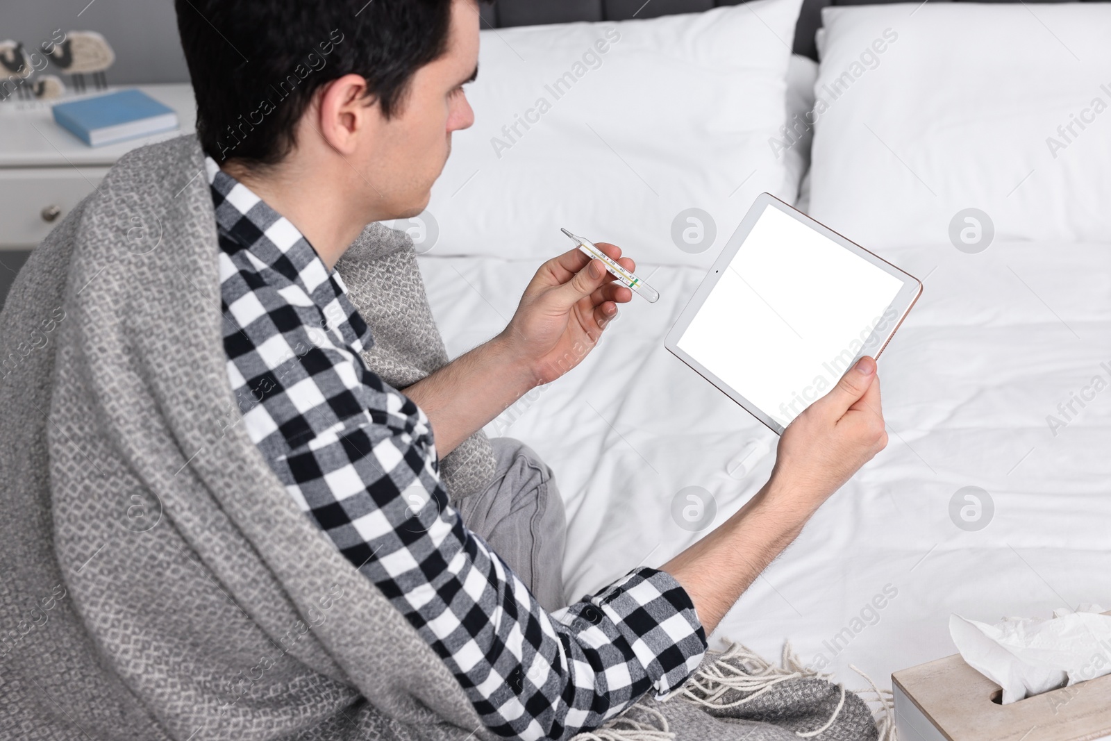 Photo of Sick man with thermometer having online consultation with doctor via tablet at home