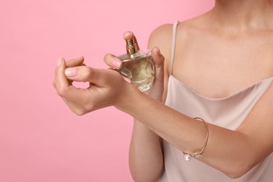 Woman spraying perfume onto wrist against pink background, closeup