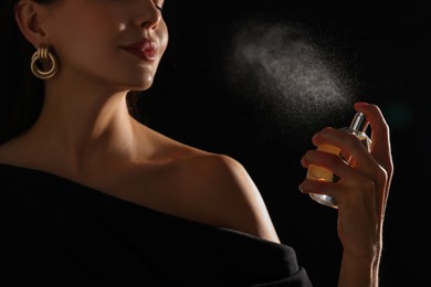 Photo of Woman spraying perfume on black background, closeup