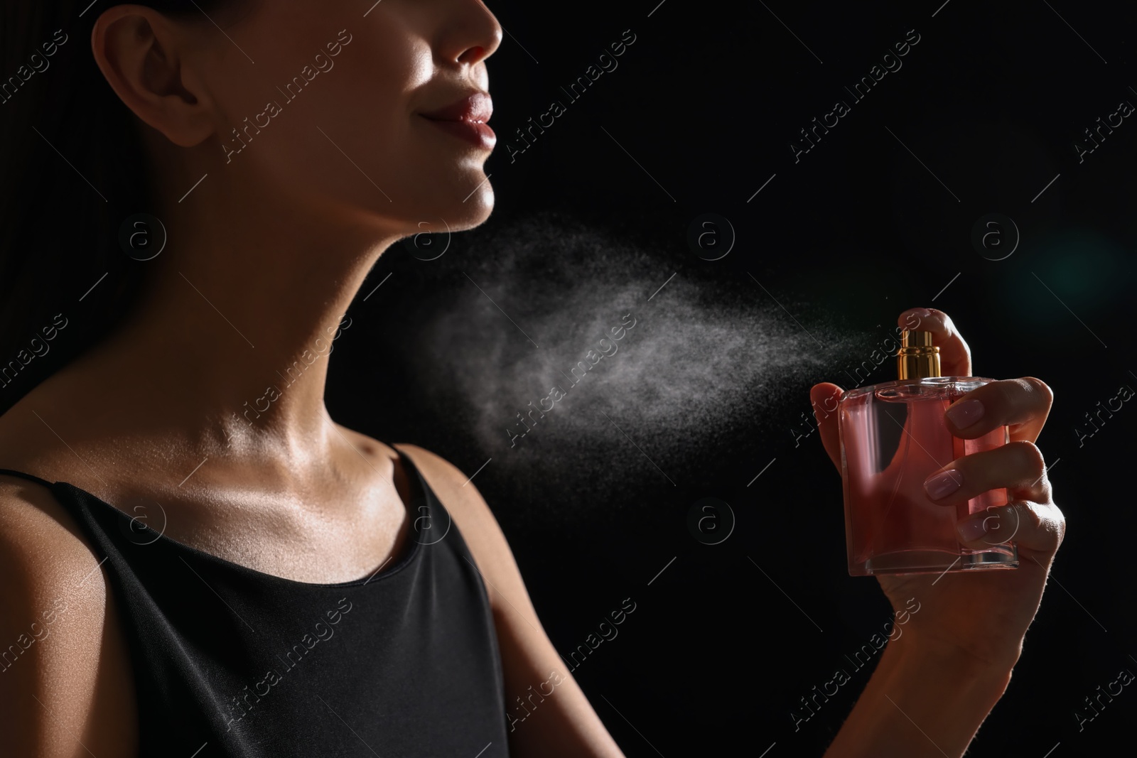 Photo of Woman spraying perfume on black background, closeup