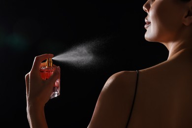 Woman spraying perfume on black background, back view