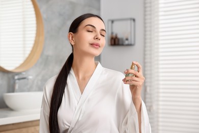 Photo of Beautiful woman spraying aromatic perfume in bathroom