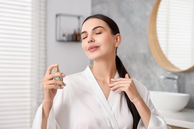 Photo of Beautiful woman spraying aromatic perfume in bathroom