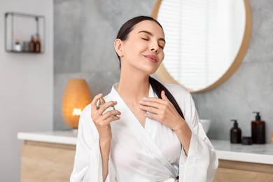 Photo of Beautiful woman spraying aromatic perfume in bathroom