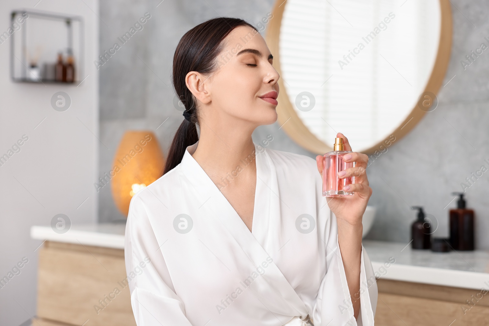 Photo of Beautiful woman spraying aromatic perfume in bathroom