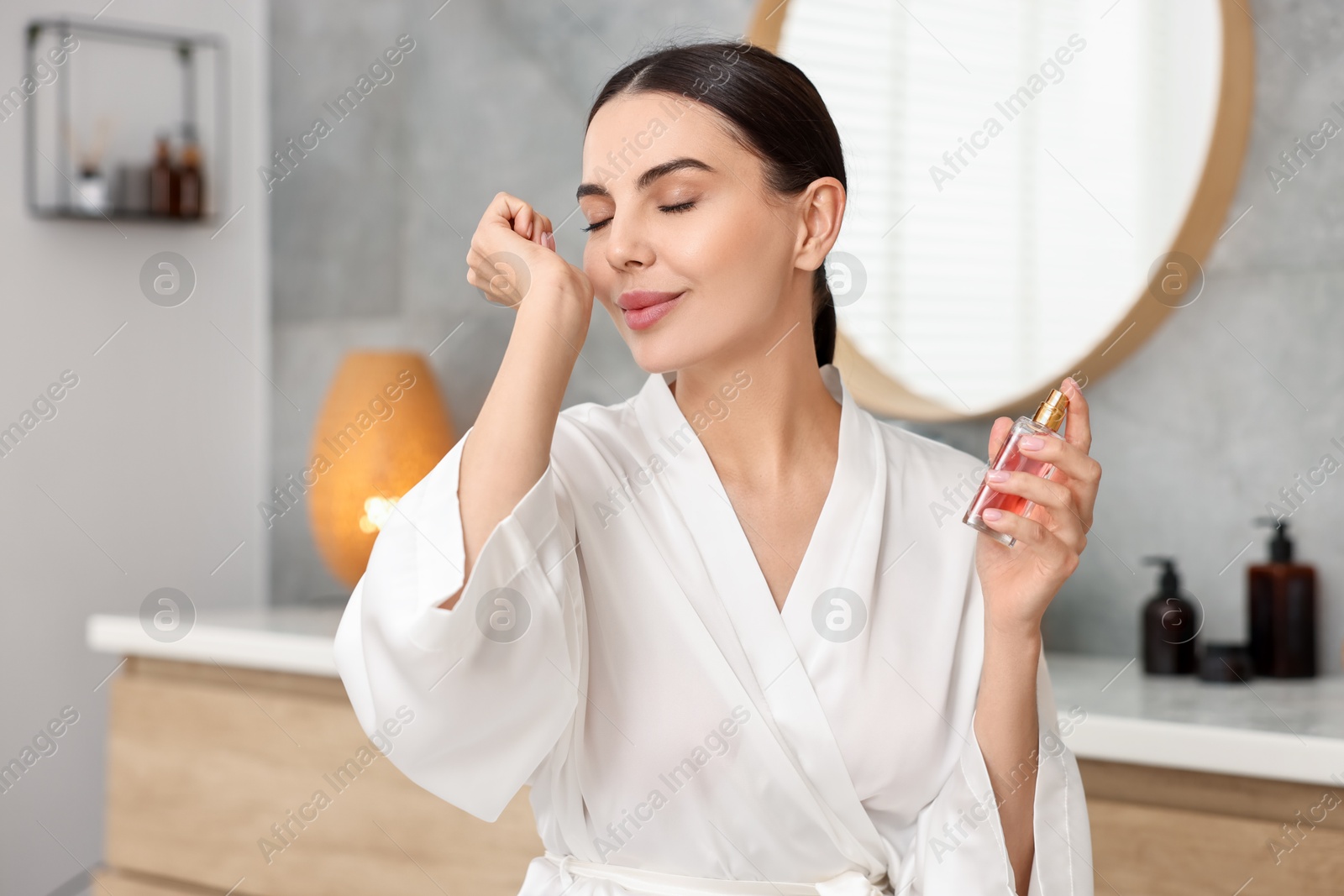 Photo of Beautiful woman smelling aromatic perfume in bathroom