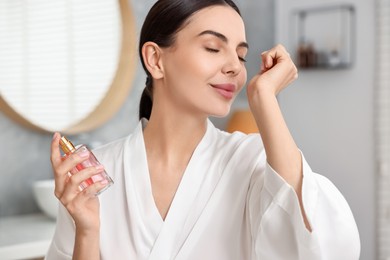 Photo of Beautiful woman smelling aromatic perfume in bathroom