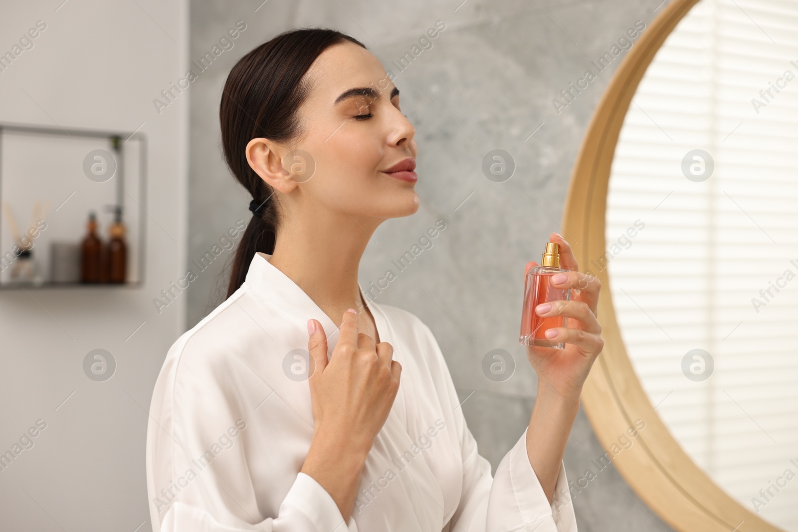 Photo of Beautiful woman spraying aromatic perfume in bathroom