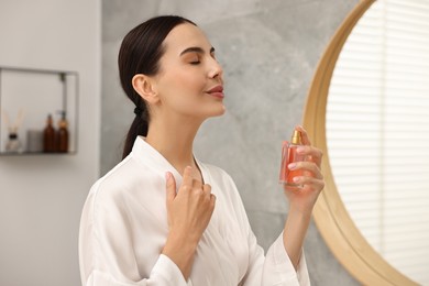 Beautiful woman spraying aromatic perfume in bathroom