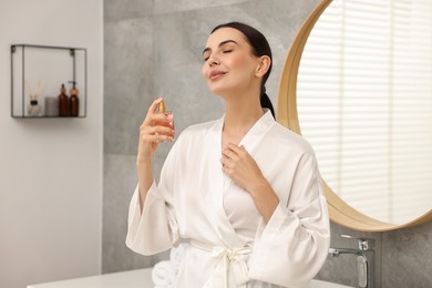 Photo of Beautiful woman spraying aromatic perfume in bathroom