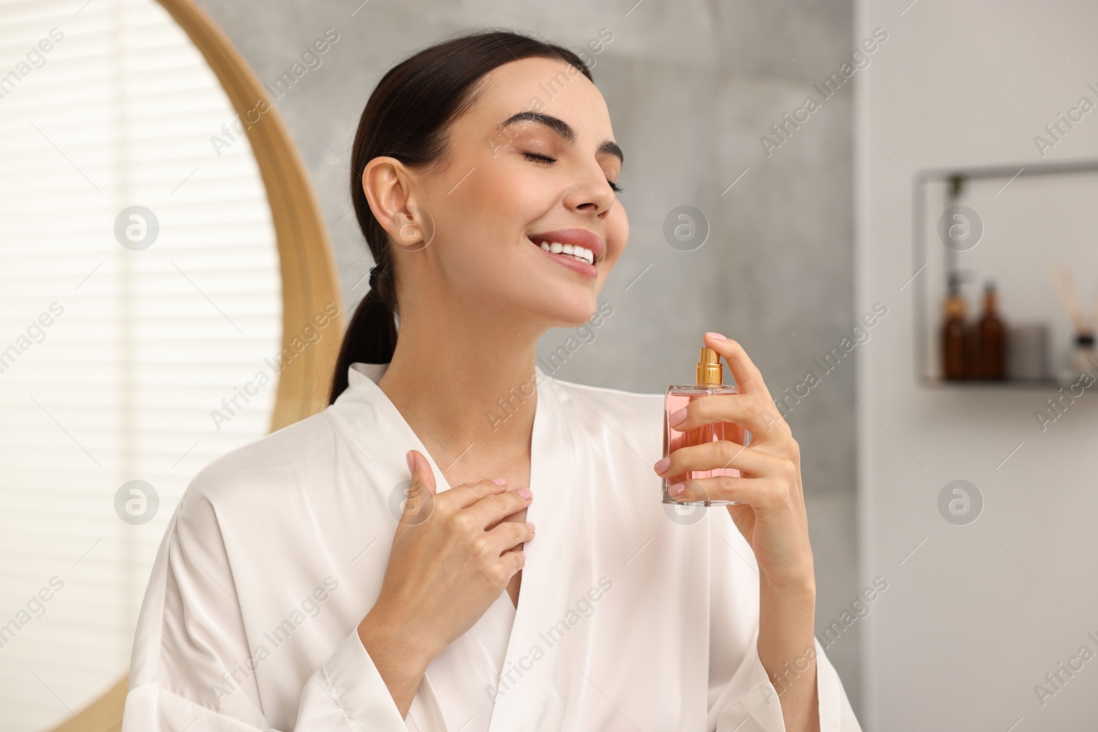 Photo of Smiling woman with bottle of perfume in bathroom