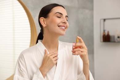 Photo of Smiling woman with bottle of perfume in bathroom