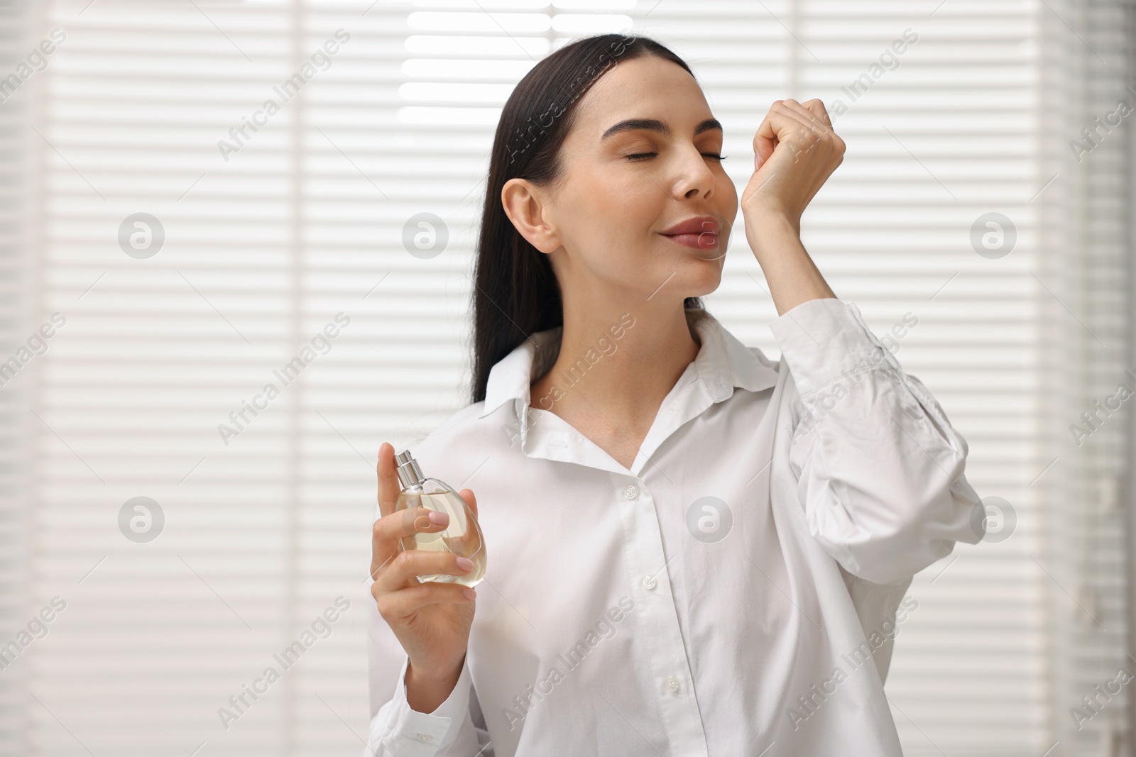 Photo of Beautiful woman smelling perfume on wrist at home