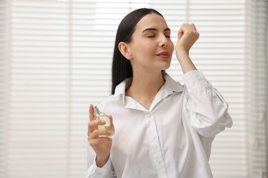 Beautiful woman smelling perfume on wrist at home