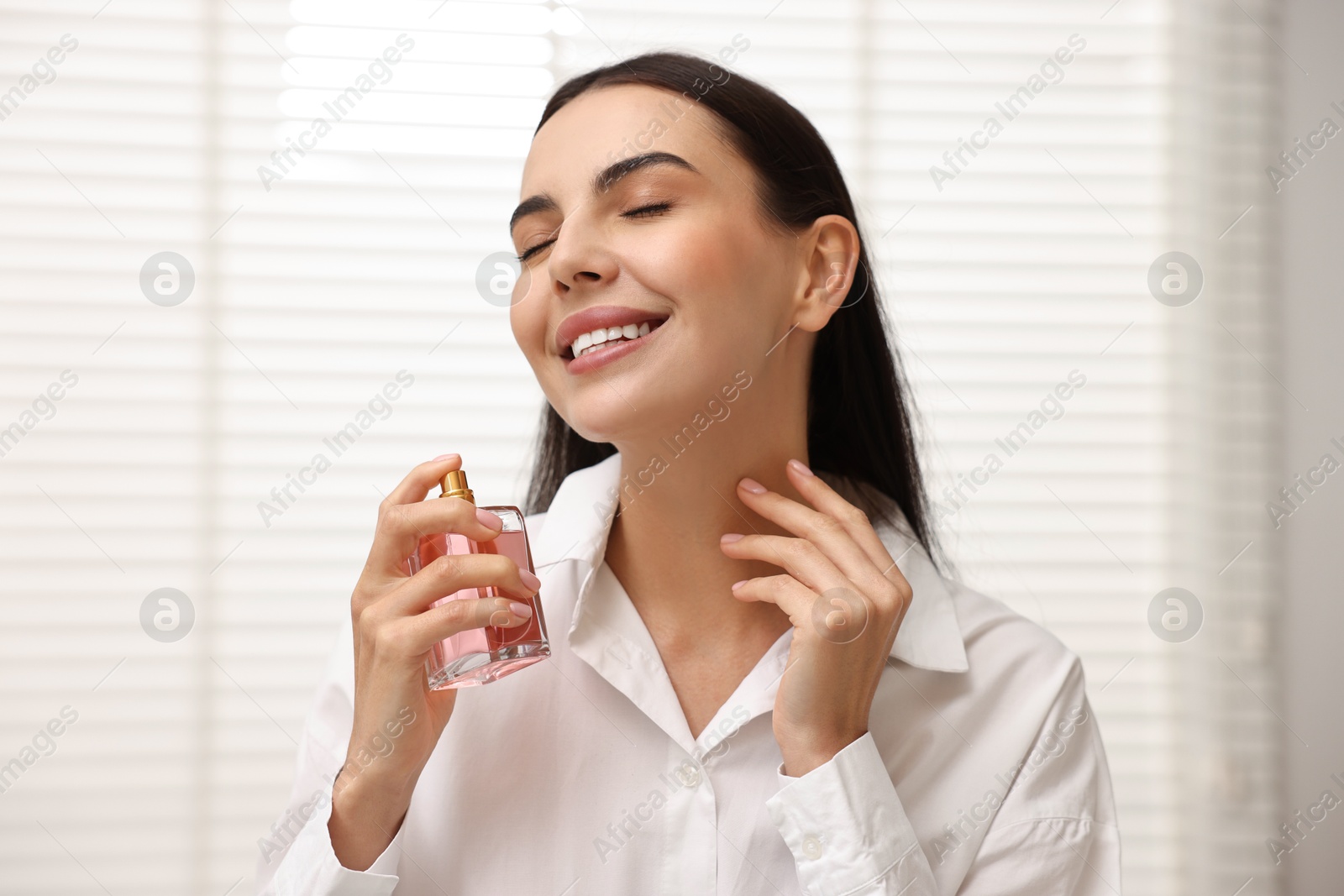 Photo of Smiling woman spraying aromatic perfume at home