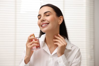 Photo of Smiling woman spraying aromatic perfume at home