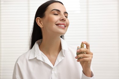 Photo of Smiling woman spraying aromatic perfume at home