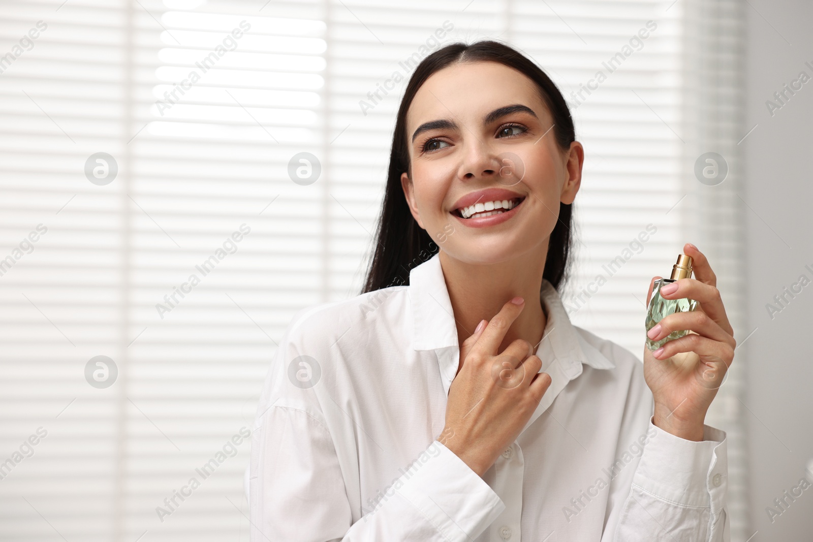 Photo of Smiling woman with bottle of perfume at home. Space for text