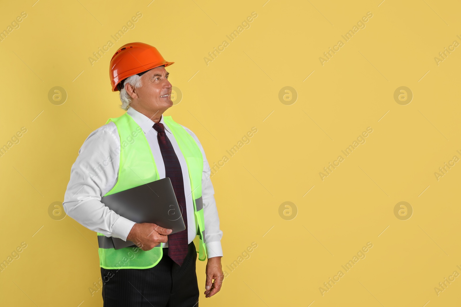 Photo of Engineer in hard hat with laptop on yellow background, space for text