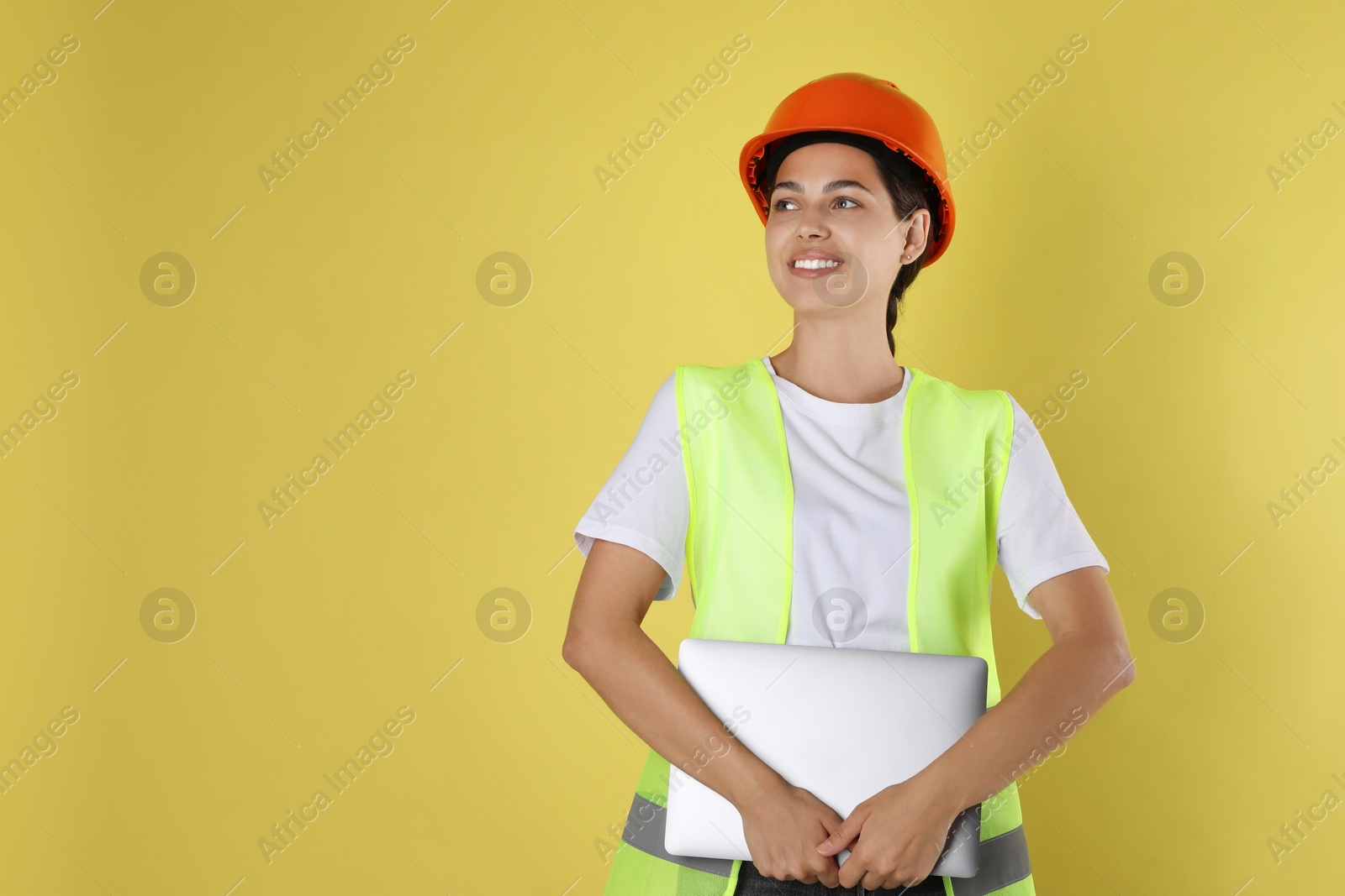 Photo of Engineer in hard hat with laptop on yellow background, space for text