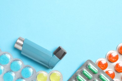 Photo of Asthma inhaler and pills on light blue background, flat lay. Space for text