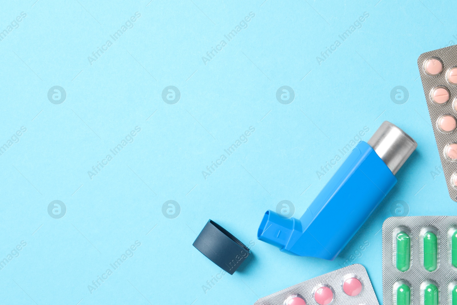 Photo of Asthma inhaler and pills on light blue background, flat lay. Space for text