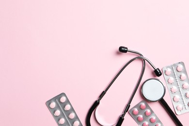 Photo of Stethoscope and pills on pink background, flat lay. Space for text