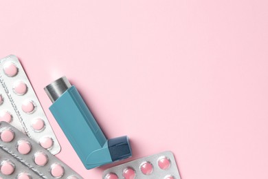 Photo of Asthma inhaler and pills on pink background, flat lay. Space for text