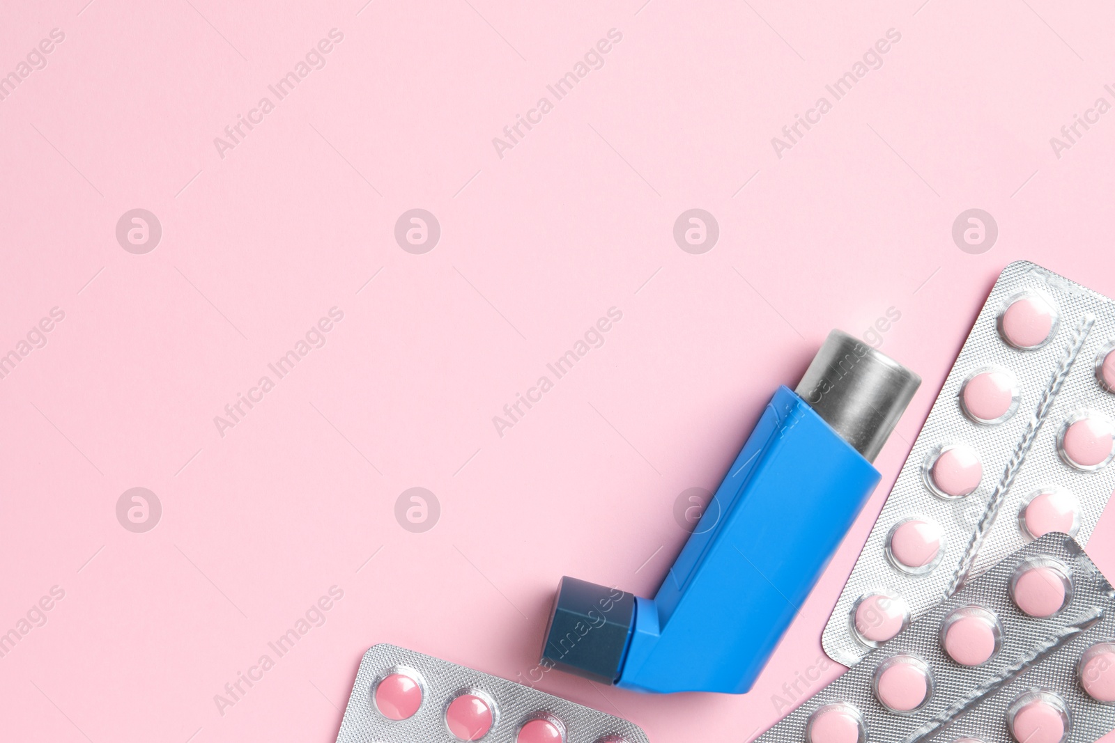 Photo of Asthma inhaler and pills on pink background, flat lay. Space for text