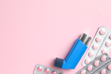 Photo of Asthma inhaler and pills on pink background, flat lay. Space for text