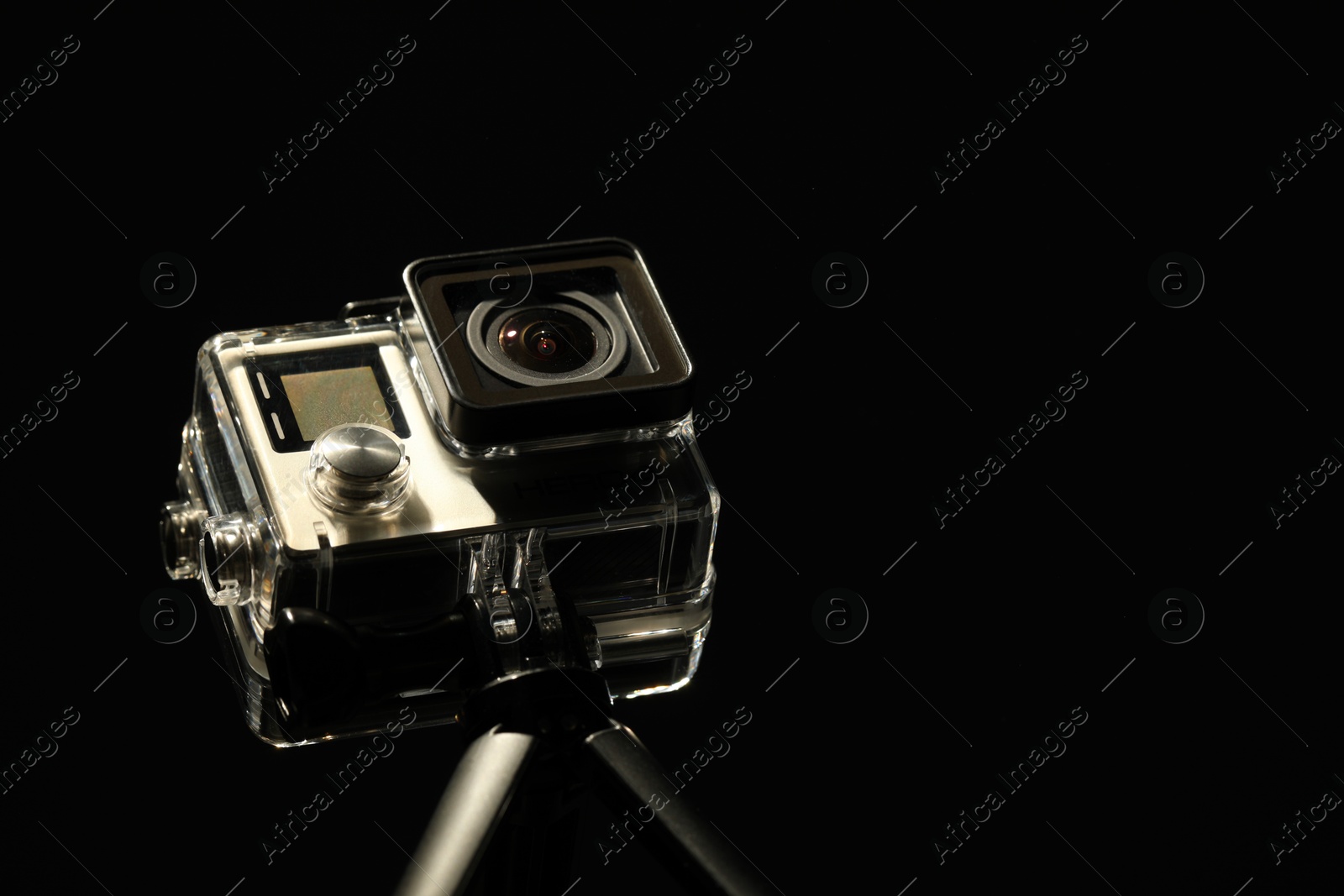 Photo of Modern action camera and tripod against black background, closeup. Space for text