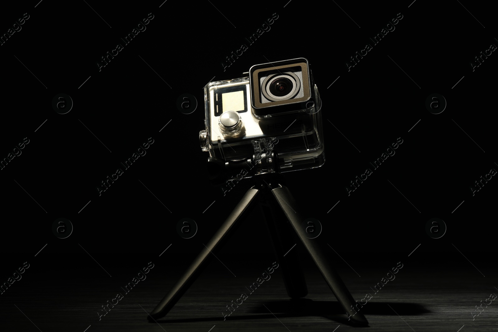 Photo of Modern action camera and tripod on wooden surface against black background