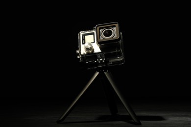 Photo of Modern action camera and tripod on wooden surface against black background