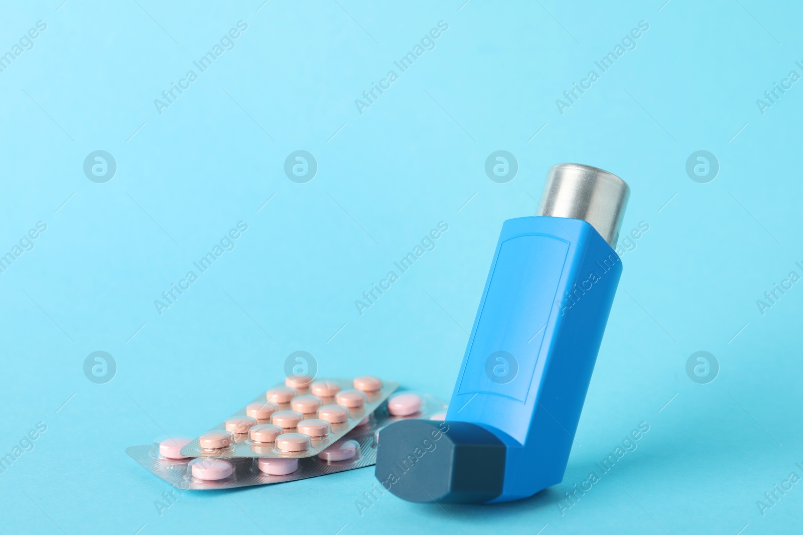 Photo of Inhaler and pills on light blue background, closeup. Asthma treatment