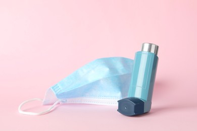 Photo of Asthma inhaler and medical mask on pink background, closeup