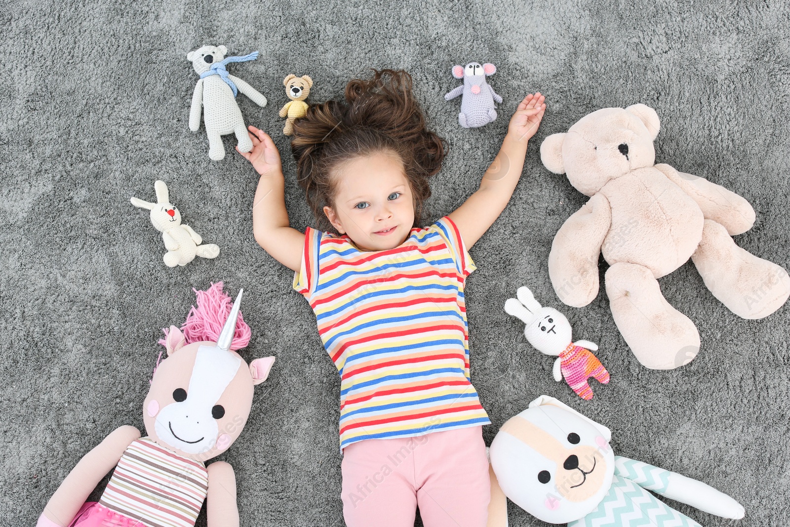 Photo of Cute little girl and soft toys on floor, top view